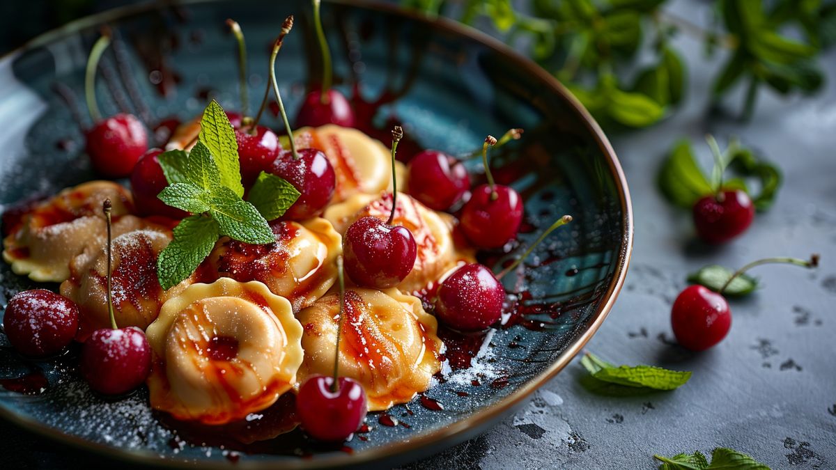 Ravioles dorées entourées de cerises rouges et de feuilles de menthe dans une assiette creuse bleu nuit