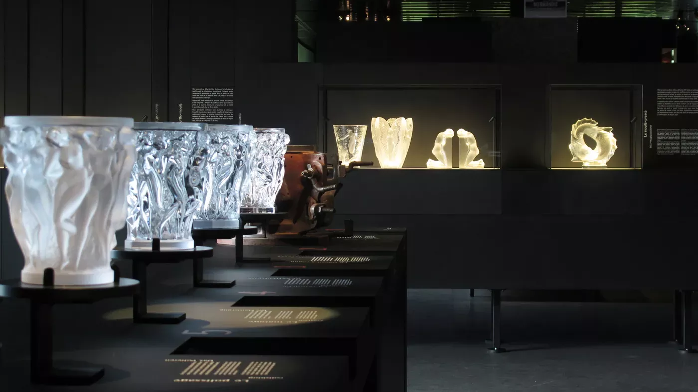 Vases en verre blanc moulé exposés sur des socles éclairés dans la salle sombre d’un musée