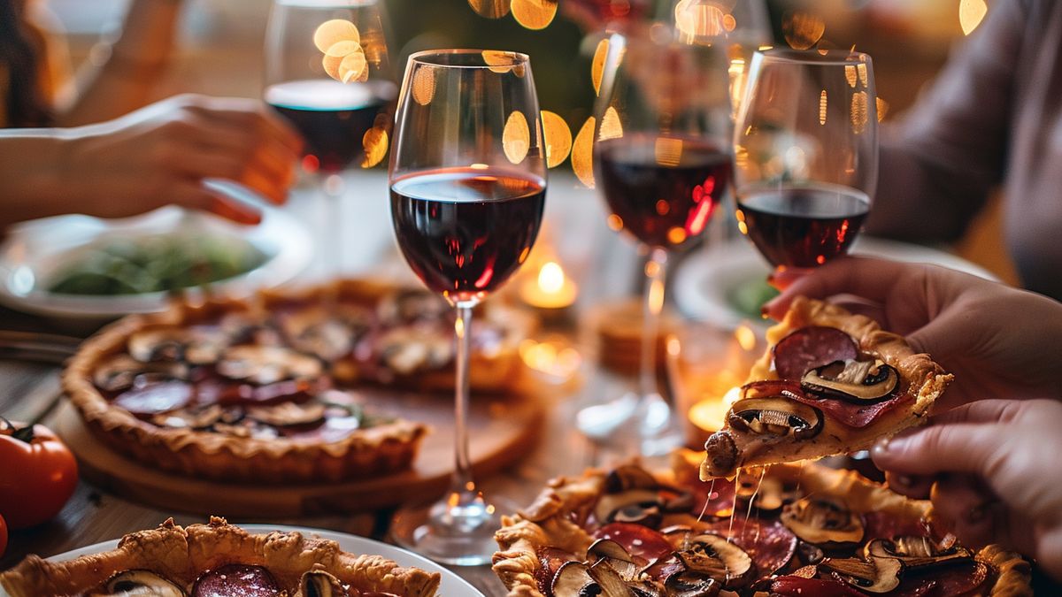 Convives partageant des pizzas rondes aux champignons et au salami avec des verres de vin rouge
