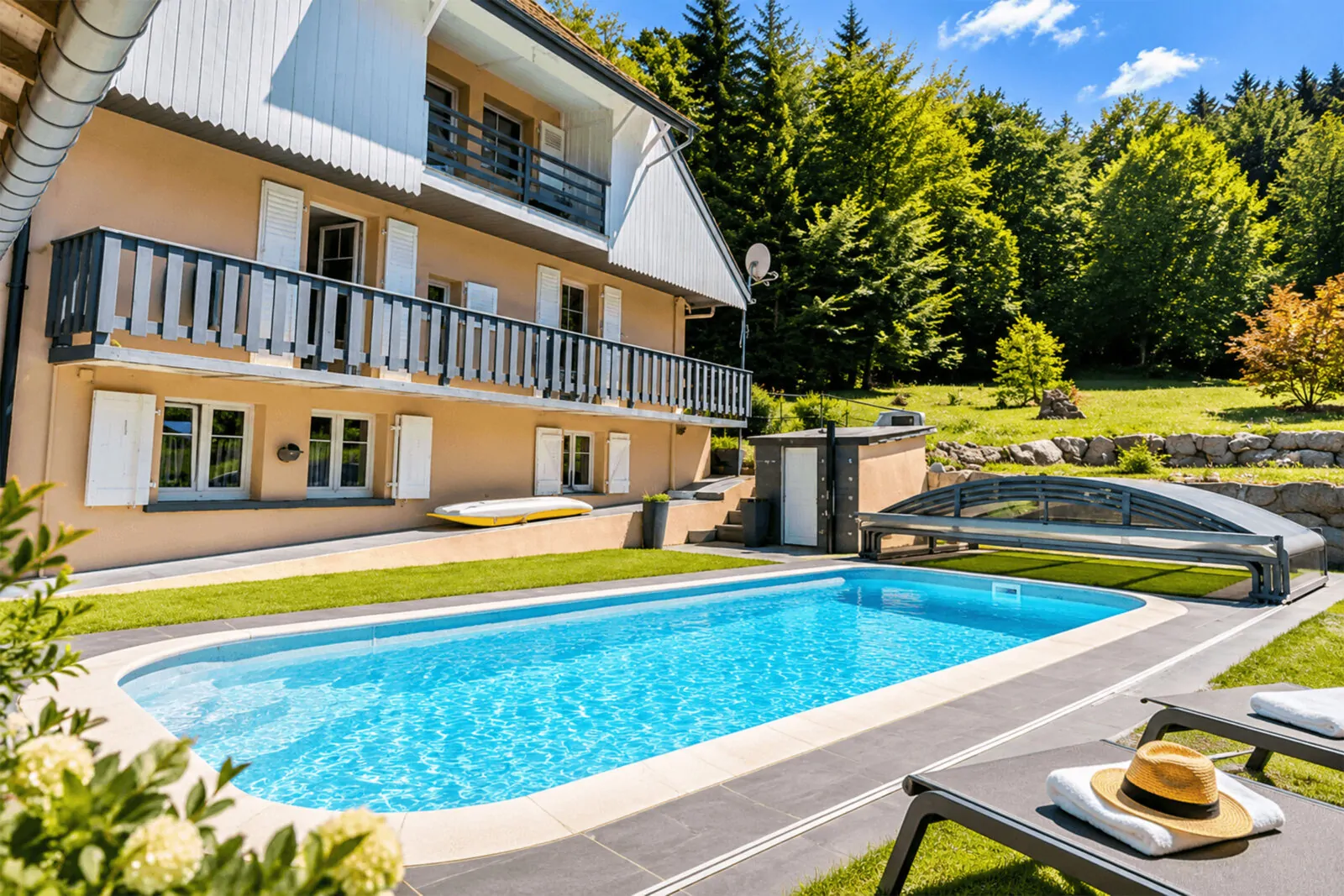Maison d’hôtes à balcon avec piscine bordée de transats, en lisière d’une forêt de sapins en été