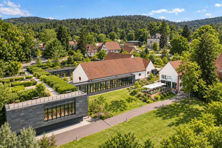 Vue aérienne du Musée Lalique, ses bâtiments modernes et ses jardins dans une vallée boisée à Wingen-sur-Moder
